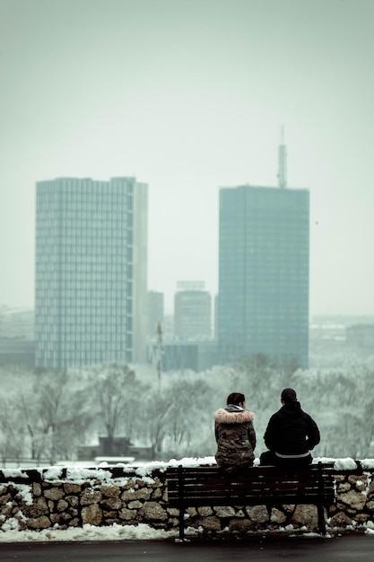 Free photo scenic shot of a heterosexual couple sitting on the bench and looking at the cityscape