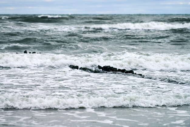 Живописный вид на синее море с пенящимися волнами. старинные длинные деревянные волнорезы, уходящие далеко в море, зимний пейзаж балтийского моря. тишина, уединение, спокойствие и покой.