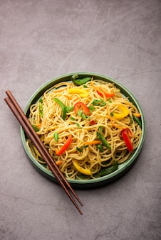 Schezwan noodles or szechwan vegetable hakka noodles or chow mein is a popular indo-chinese recipes, served in a bowl or plate with wooden chopsticks Free Photo