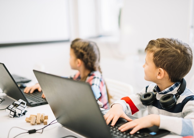 School children sitting with laptop looking at blackboard