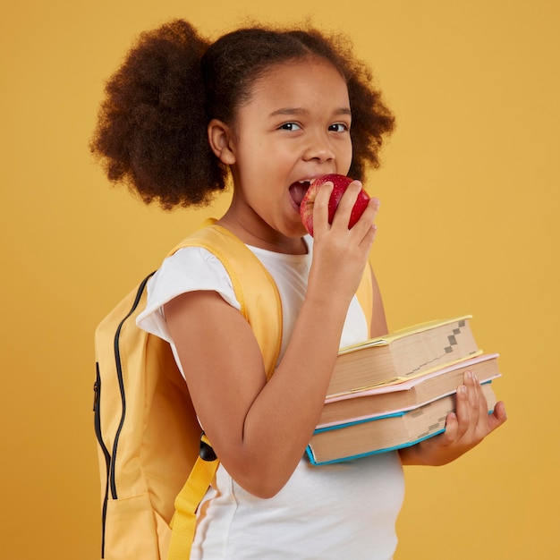 Foto gratuita ragazza della scuola che mangia una mela e che tiene i libri