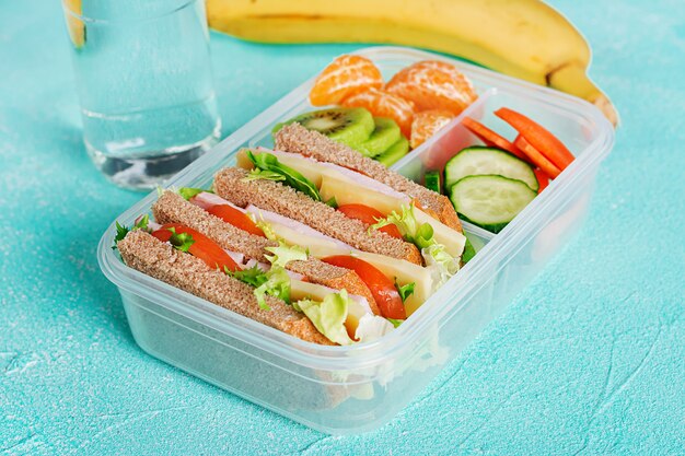 샌드위치, 야채, 물, 과일 테이블에 학교 점심 상자.