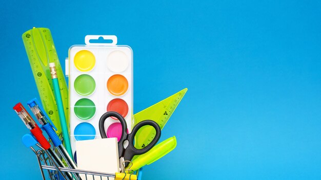 School stationery in a toy shopping cart on a blue background. The concept of preparing for the beginning of the school year. Copy space