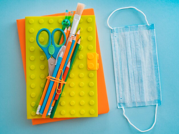 School supplies with medical face mask on blue blue. Flat lay, top view, layout, template, free space