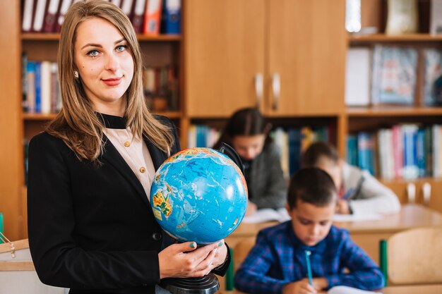 School teacher with globe on background of studying pupils