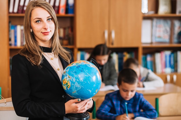 School teacher with globe on background of studying pupils