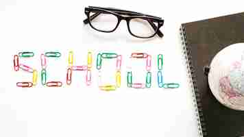 Free photo school word made up of paper clips near spiral notepad; globe and spectacles on white surface