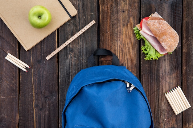 Free photo schoolbag, sandwich and stationery on table