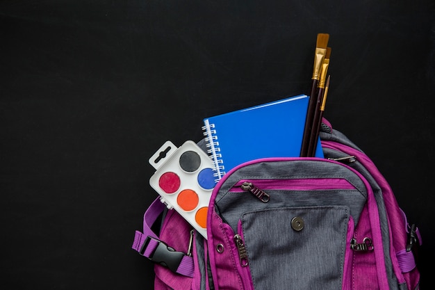 Free photo schoolbag with brushes, watercolors and copybook