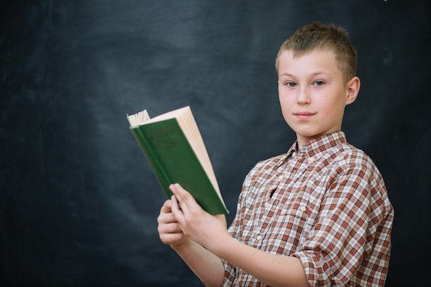 Free photo schoolboy holding book at chalkboard