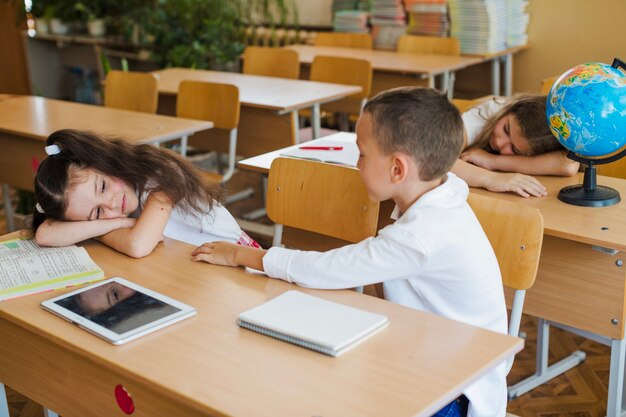 Schoolboy sitting in classroom with sleeping schoolgirls