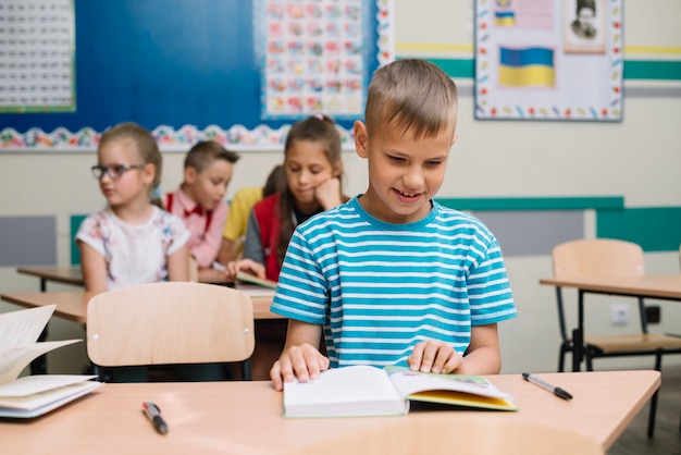 Free photo schoolboy with book at desk