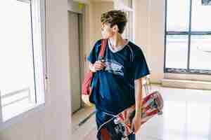 Free photo schoolboy with skateboard in building