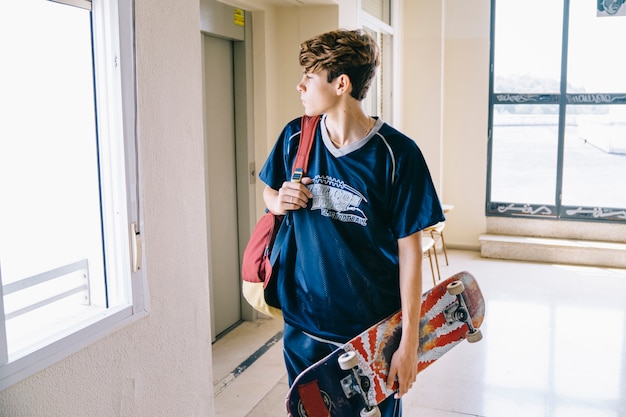 Schoolboy with skateboard in building