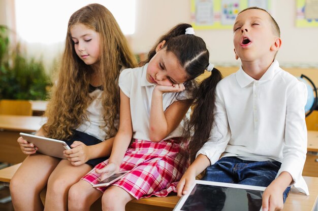 Schoolchildren napping on table holding gadgets