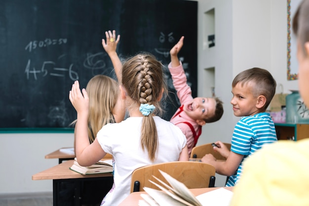 Schoolchildren sitting in classroom raising hands