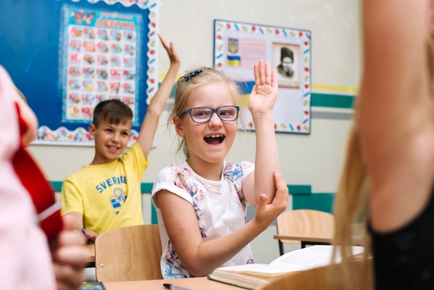 Free photo schoolchildren sitting at lesson holding hands up