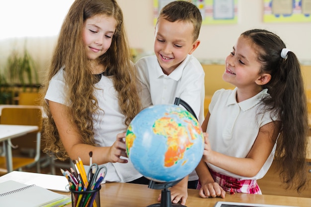 Schoolchildren studying globe standing in classroom