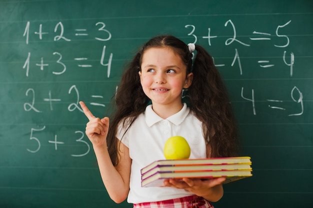 Free photo schoolgirl pointing up at blackboard