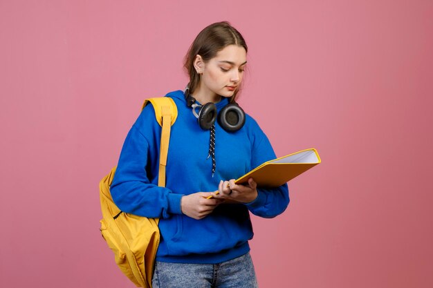 Schoolgirl with earphones standing holding yellow folder reading