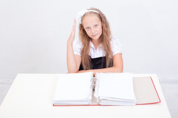 Schoolgirl  with red folders sitting at the table over white background