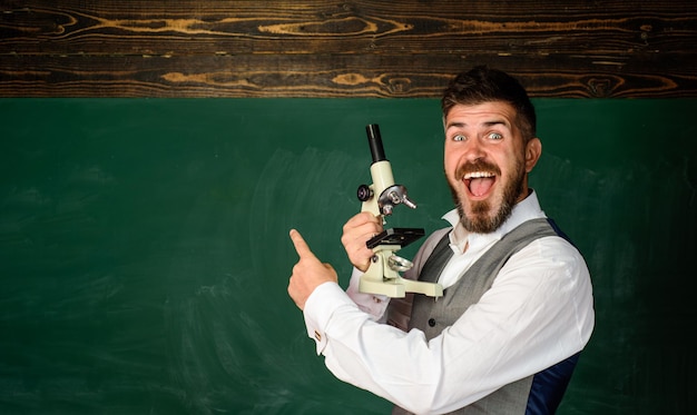 Scientifics research male scientist holds microscope teacher with microscope near chalkboard copy