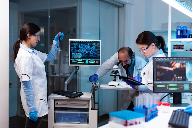 Scienziato che analizza il campione di sangue in vacutainer con il team di ricerca che guarda attraverso il microscopio