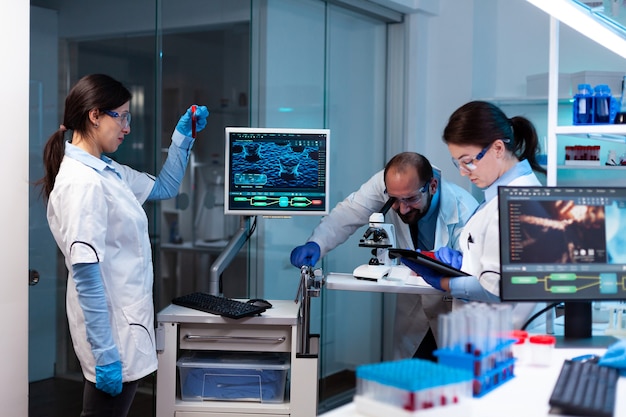 Free photo scientist analyzing blood sample in vacutainer with researching team looking through microscope