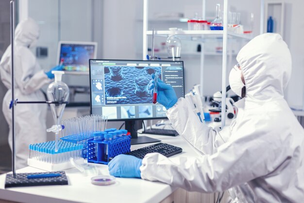 Scientist checking tube with blood analysis dressed in ppe during coronavirus epidemic