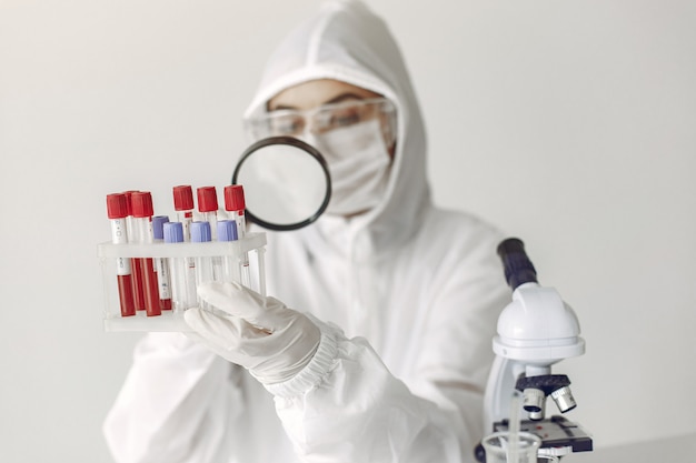 작업복 의류의 과학자가 실험실에서 코로나 바이러스 샘플을 검사하고 있습니다.