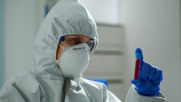 Scientist in coverall doing research analysing liquid in tube at modern equipped laboratory. Biochemist examining vaccine evolution using high tech for treatment development against covid19 virus