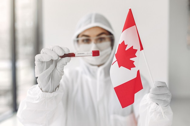 コロナウイルスのサンプルとカナダの旗を持つつなぎ服の科学者