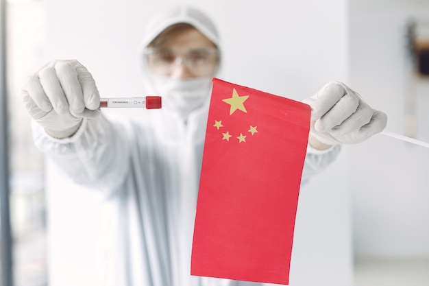 コロナウイルスのサンプルと中国の旗を持つつなぎ服の科学者