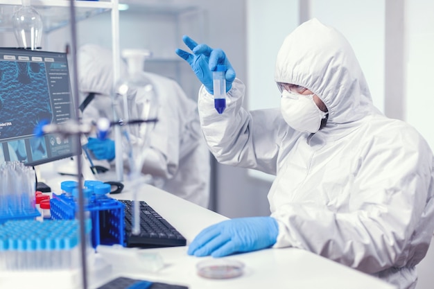 Scientist in lab coversall looking closely at sample in test tube in the course of coroanvirus