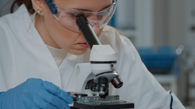 Scientist looking through microscopic lens to work on experiment, using microscope to analyze dna with selective focus in laboratory. Biologist working with magnifying glass. Close up