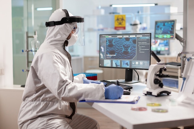 Ученый в костюме ppe делает заметки в буфере обмена, работая над лечением вирусов