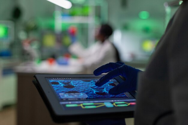 Scientist researcher doctor analyzing genetic mutation test using tablet while her collegue typing biological expertise on computer