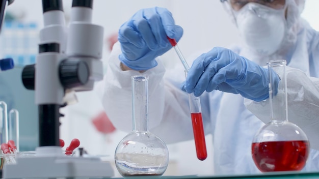 Scientist researcher doctor with ppe equipment holding test tubes analyzing blood sample working at vaccine development during microbiology experiment in hospital laboratory. Medicine concept