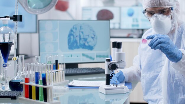 Scientist researcher holding medical slide analyzing blood sample writing medical expertise on clipboard. Chemist doctor working at coronavirus vaccine during chemistry experiment in laboratory