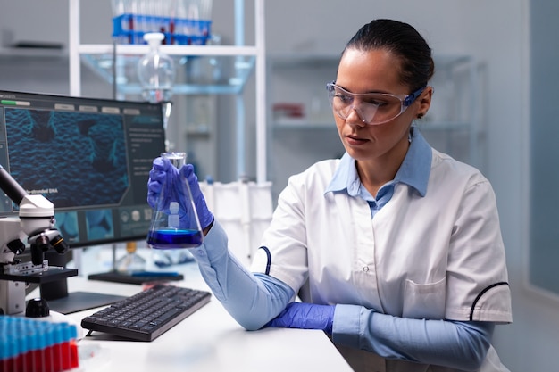 Scientist woman doctor holding glass flask analyzing liquid solution