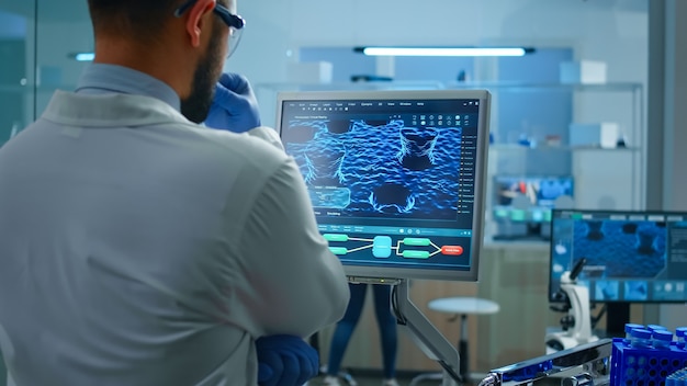 Scientist working in laboratory analysing test trial vaccine checking drug data standing in front of pc