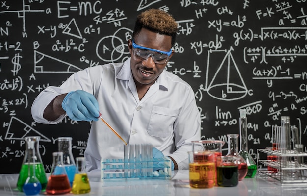 科学者は実験室でオレンジ色の化学物質をガラスに落とす