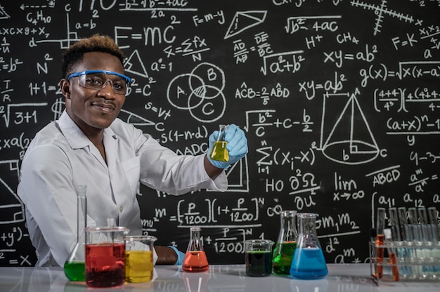 과학자들은 실험실에서 행복하게 안경을 쓰고 손으로 노란색 화학 물질을 처리합니다.