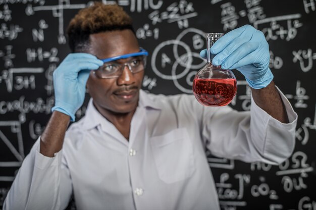 科学者は実験室でガラス中の赤い化学物質を見て、ガラスを手で処理します