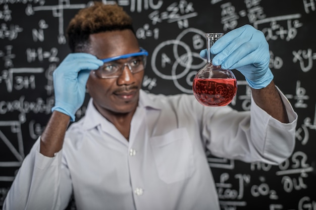 Ученые смотрят на красный химикат в стакане в лаборатории и вручную обрабатывают очки
