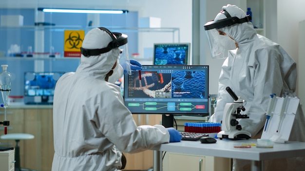 Free photo scientists in protection suits analysing test tubes with blood sample in chemical equipped laboratory. biologists examining vaccine evolution using high tech and technology researching treatment