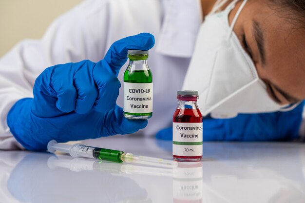 Ученые в масках и перчатках несут флаконы с вакцинами для защиты Covid-19