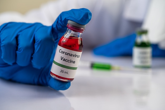 Ученые в масках и перчатках несут флаконы с вакцинами для защиты Covid-19