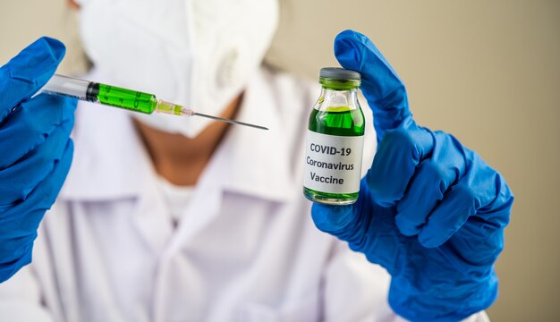 마스크와 장갑을 착용하는 과학자 covid-19를 예방하기 위해 백신으로 주사기를 들고