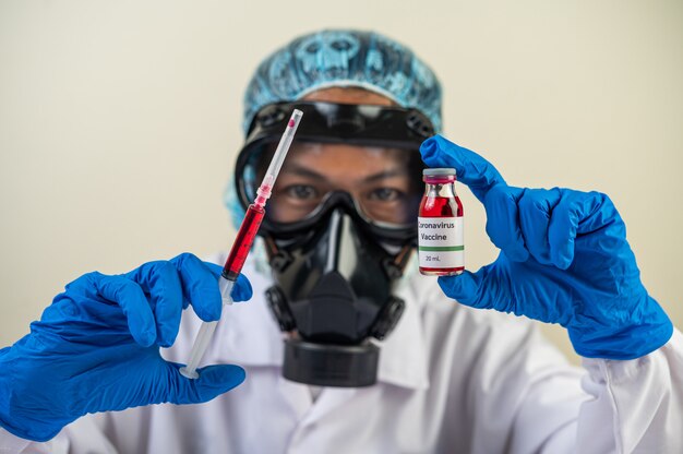 Ученые в масках и перчатках держат шприц с вакциной для профилактики коид-19